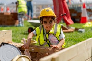 Child in a high vis and hard hat plays in the sandpit