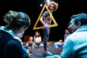 Image of actress holding a yellow triangle over her shoulder with families in the background.