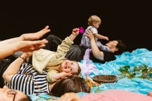Mother laying down on the floor of a baby show holding her toddler who is clutching a pink feather.