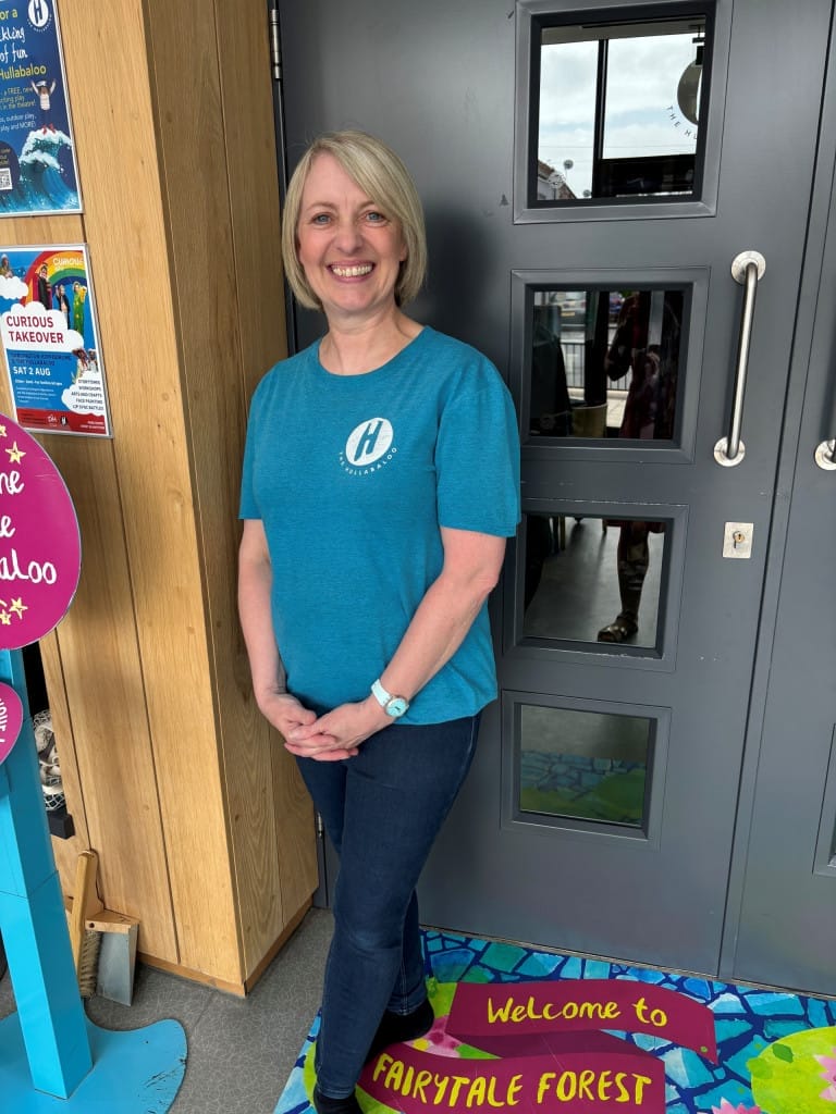 A friendly member of staff in a blue Theatre Hullabaloo t-shirt is standing at the entrance and smiling at the camera