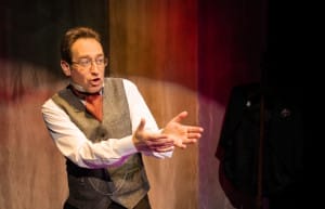 Chris the storytelling is wearing glasses, a white shirt and a tweed waistcoat with an orange neckerchief.