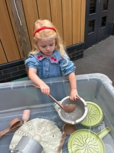 Little girl in denim dress plays in the water tray