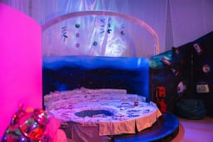 A sensory room with a comfy moon covered in white material, with purple lights