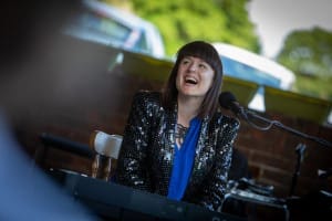 Bridie, a singer, sits at her piano in a sparkly jacket laughing