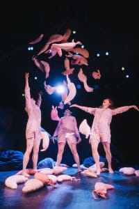 3 actors throwing sausage shape cushions in the air