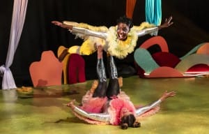 An actress flying on the legs of another actress laying on the floor.