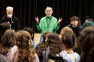 Jessica wearing a green jumper smiling, delivering a workshop to a group of children