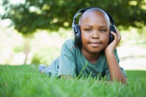 Little boy lying on grass wearing headphones and smiling on a sunny day