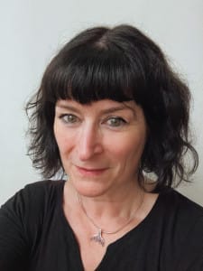 Emma Rees, the new executive director of Theatre Hullabaloo - A white women, with shoulder length curly hair and a silver necklace